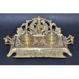 A Victorian cast brass desk top ink stand, arching pierced pen rest back, two hinged inkwells,