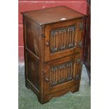 An oak bedside cabinet in the monastic taste two linenfold doored cupboards. 70cm high x 40.