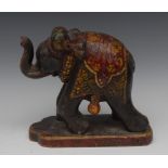 An Indian carved and painted model, of an elephant, standing, with trunk raised, shaped base,