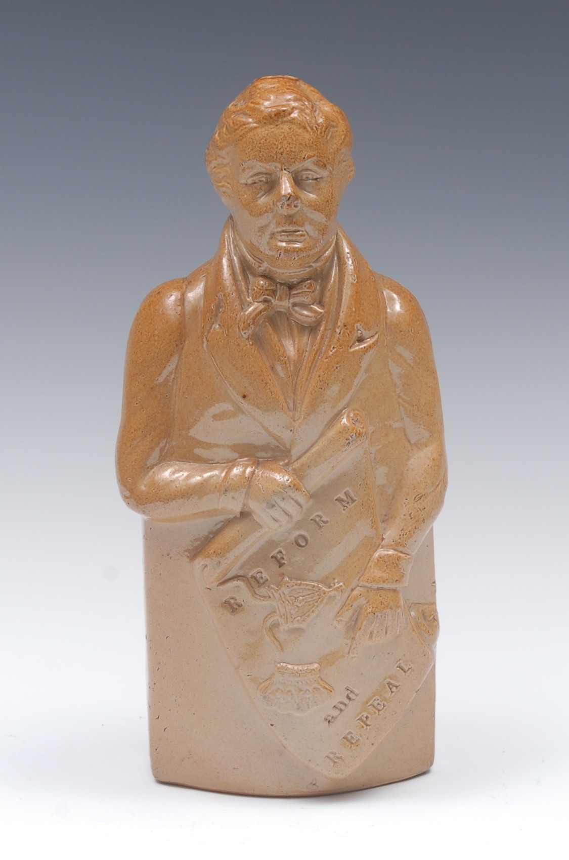 A 19th century brown salt glazed stoneware figural flask, of Robert Peel, holding a scroll,