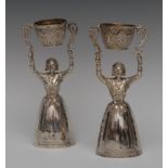 A pair of Elizabeth II silver wager cups, in Dutch style, each as a lady holding aloft a tumbler,