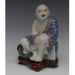 A Chinese Buddha, seated, his hands clasping his knee, in colours, hardwood stand,