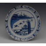 A Delft circular plate, decorated in underglaze blue with stylised sampans, hut and island,