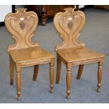 A pair of mahogany shield back hall chairs, heraldic cartouche, wooden seat,