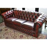 An executive office ox blood leather button upholstered three seat Chesterfield settee.