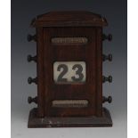 An early 20th century oak perpetual desk calendar, sarcophagus cresting above apertures for day,