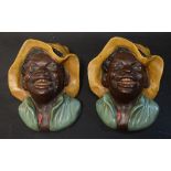 A pair of Bretby wall pockets, modelled as widely grinning Negro boys, yellow sunhats,