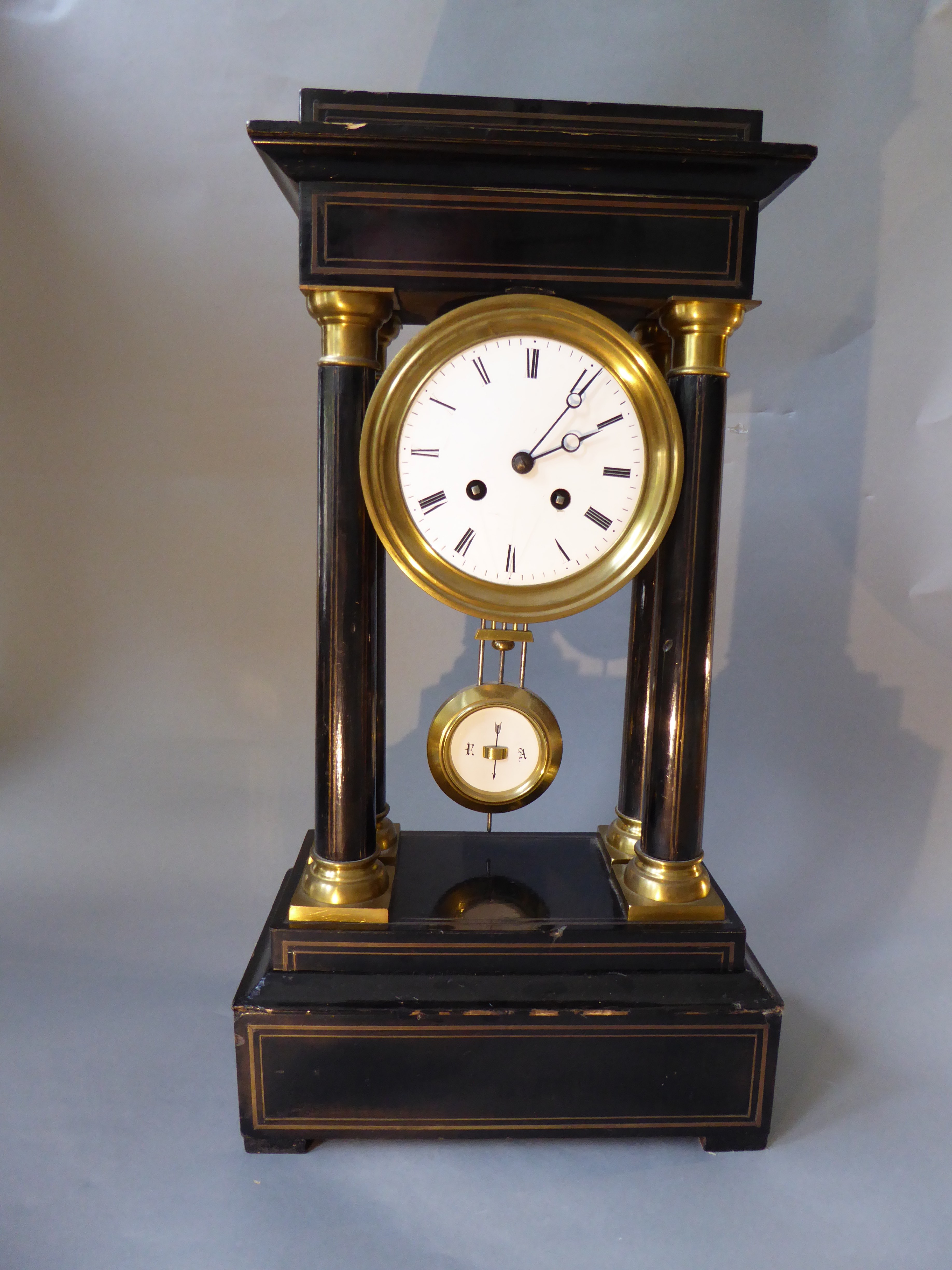 A Portico clock, in ebonised wood, columns with brass bases and capitals, enamel dial & pendulum