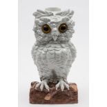 A Continental porcelain 'owl' table lamp: with inset glass eyes modelled standing on a log,