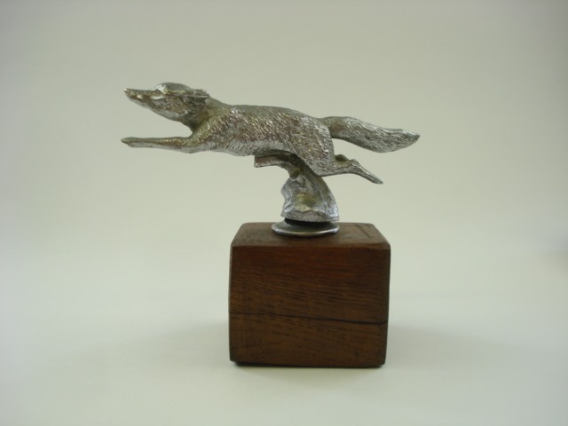 An aluminium car mascot in the form of a running fox:, unsigned , on a later wooden base, 14cm high.