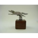 An aluminium car mascot in the form of a running fox:, unsigned , on a later wooden base, 14cm high.