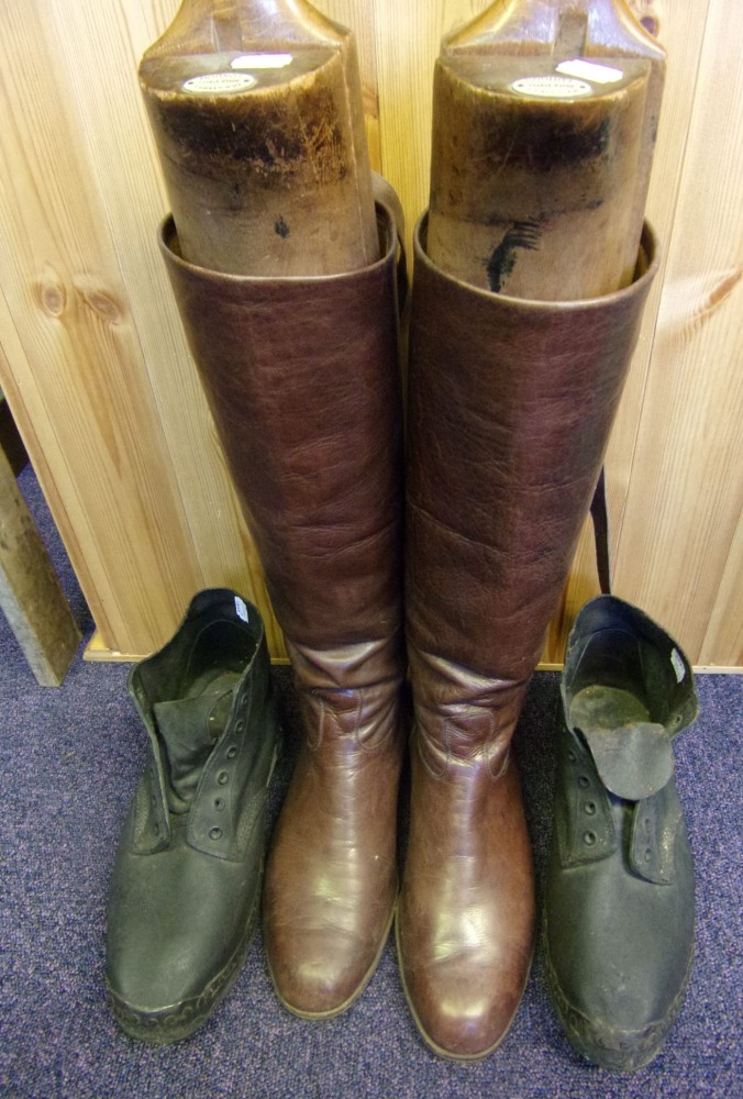 A pair of brown leather riding boots: with wooden trees and a pair of black leather clogs.