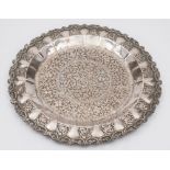 An Indian silver tray: of circular outline, decorated with scrolling foliage and flowerheads,