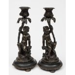 A pair of 19th century bronze figural candlesticks: depicting putti seated below flowering stems