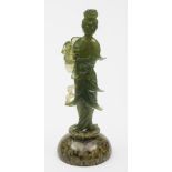 A Chinese carved green hardstone figure of a female Immortal: holding a fruiting peach branch and