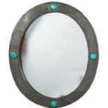 An Arts & Crafts period beaten pewter wall mirror: the oval mirror plate enclosed by a frame with