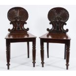 A pair of Regency carved mahogany hall chairs:, with reeded shell and scroll backs,