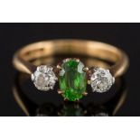 A demantoid garnet and diamond three stone ring: the central oval demantoid garnet approximately