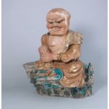 A Japanese decorated stoneware figure of a seated man: with grotesque frowning face,