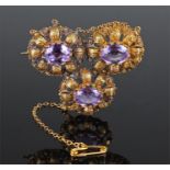 Yellow metal amethyst set brooch, the three amethyst set within curled leaf and flower head