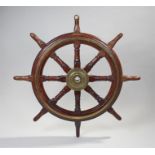 A teak, brass mounted ship's wheel, with eight turned spokes and the central boss cast with `