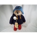 Paddington Bear - a stuffed toy, with pale blue felt hat, dark blue coat and red boots,