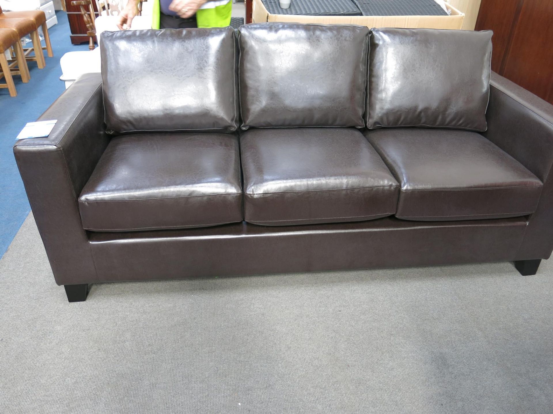 * An as new three seater sofa. The faux pu leather upholstery is brown in colour. Please note