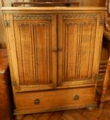 Reproduction oak cabinet with linenfold carved doors, drawer below, on bun feet,