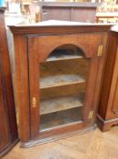 A 19th century oak glazed corner cupboard, the arched panel door enclosing three shelves,