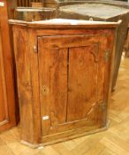 An early 19th century elm corner cupboard, the panel door enclosing three shaped shelves,