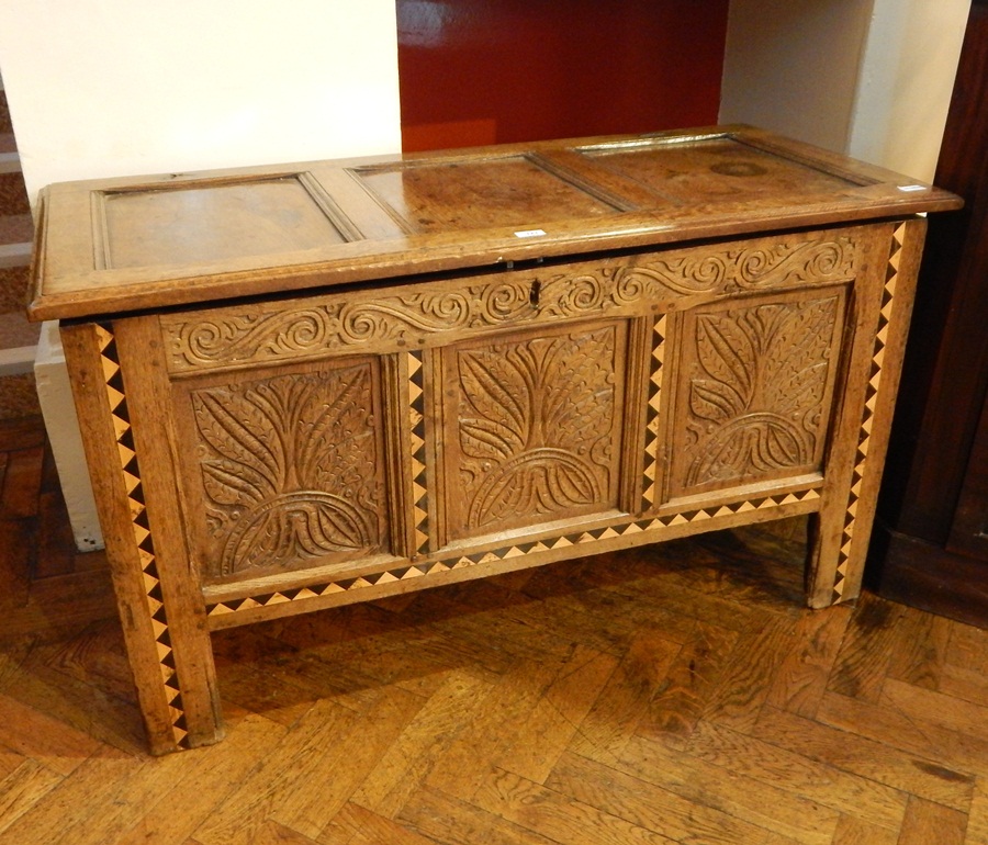 An old oak coffer, with three panel top, carved scrollwork frieze with foliate carved front panels,