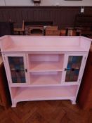 A pink painted Edwardian open bookcase, with a pair of coloured glass leaded light panelled doors,