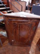An early 19th century elm corner cupboard, the panel door enclosing three shaped shelves,