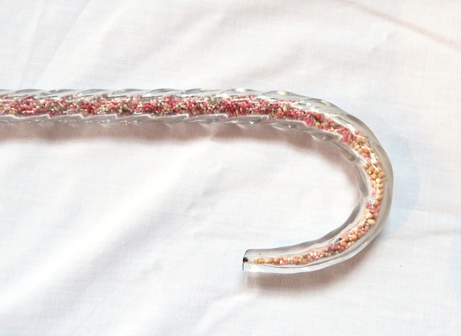 A glass walking cane, the tapering cane filled alternately with coloured sugar beads in pink,