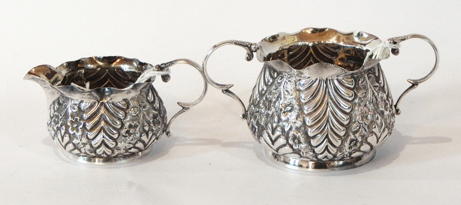 A Victorian silver two-handled sugar bowl with foliate repousse decoration with a matching cream