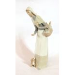 A Lladro figure of a woman wearing a wimple, carrying a basket of bread with a puppy at her feet,