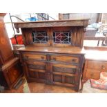 An oak court cupboard with foliate carved frieze with glazed leaded lights and panels to cupboards,