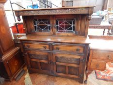 An oak court cupboard with foliate carved frieze with glazed leaded lights and panels to cupboards,