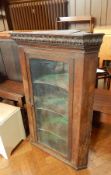 An oak corner cupboard with glazed front and three shelves, acanthus frieze decoration,