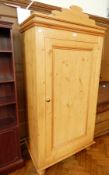 A pine single wardrobe with shaped pediment, the panel door enclosing shelf and hanging space,