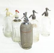 Five vintage soda syphons, one labeled "C & C Club Soda Water" and one with plaited metal casing.