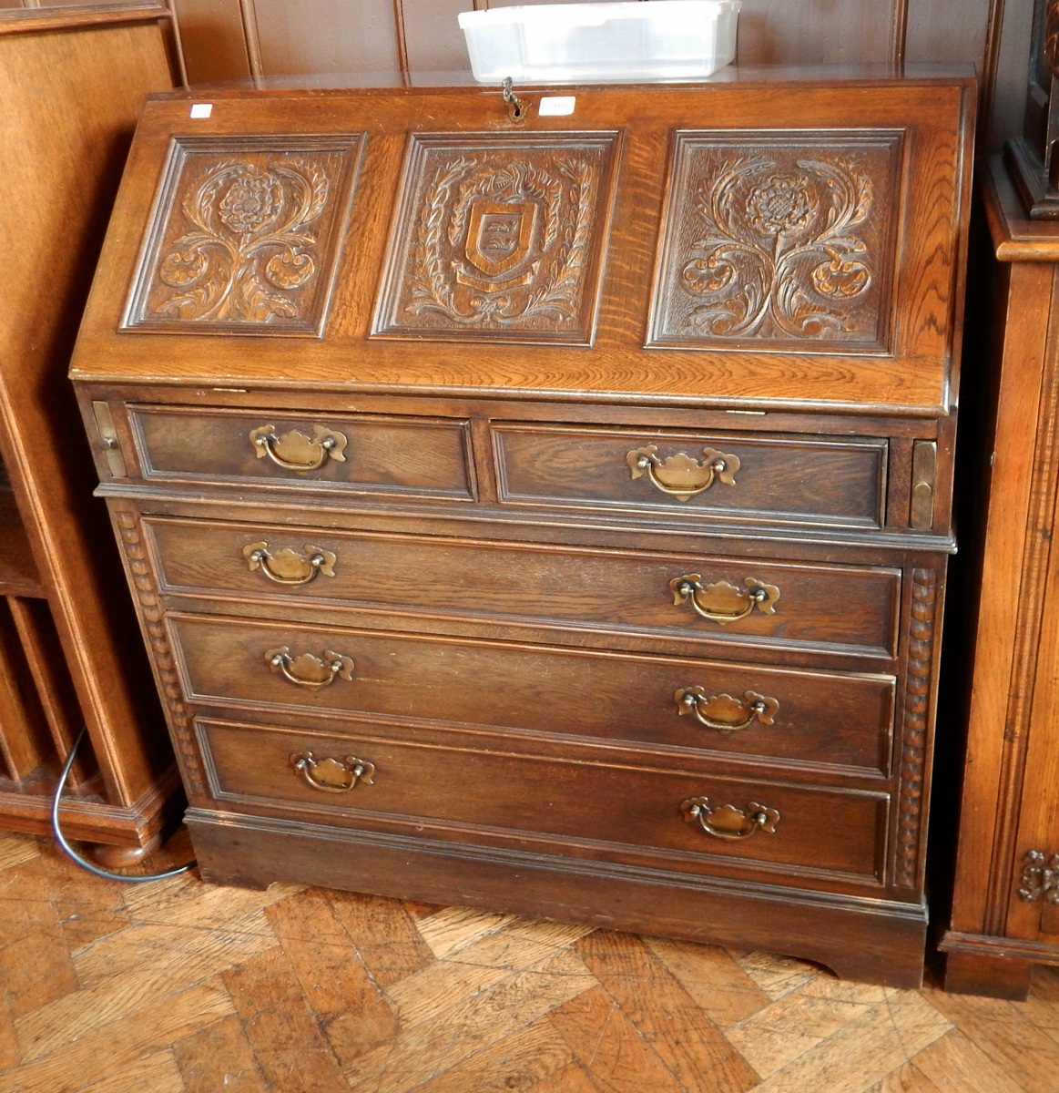 A Victorian oak bureau with two floral carved panels and coat of arms,