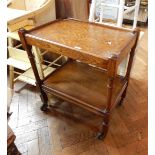 A mahogany two-tiered tea trolley on cylindrical and block supports, wheels,