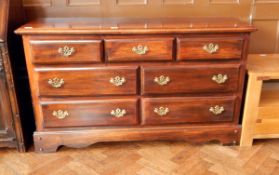 A stained wood low dresser with three short and four long drawers with swan neck handles,