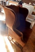 An antique wing back armchair with brown dralon, on block supports united by H-stretcher,