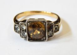 A gold ring set with a central yellow/brown zircon and the stepped shoulders with white-coloured