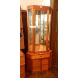A modern teak glazed corner cupboard with mirror back and glass shelves,