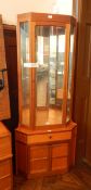 A modern teak glazed corner cupboard with mirror back and glass shelves,