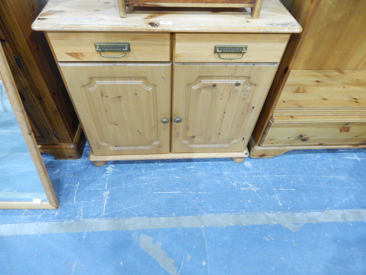 A dwarf pine cupboard fitted two drawers over two panelled doors and on bun feet,