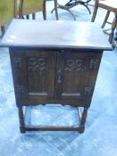 A dwarf oak cabinet enclosed by two carved gothic-style carved panelled doors, on turned supports,